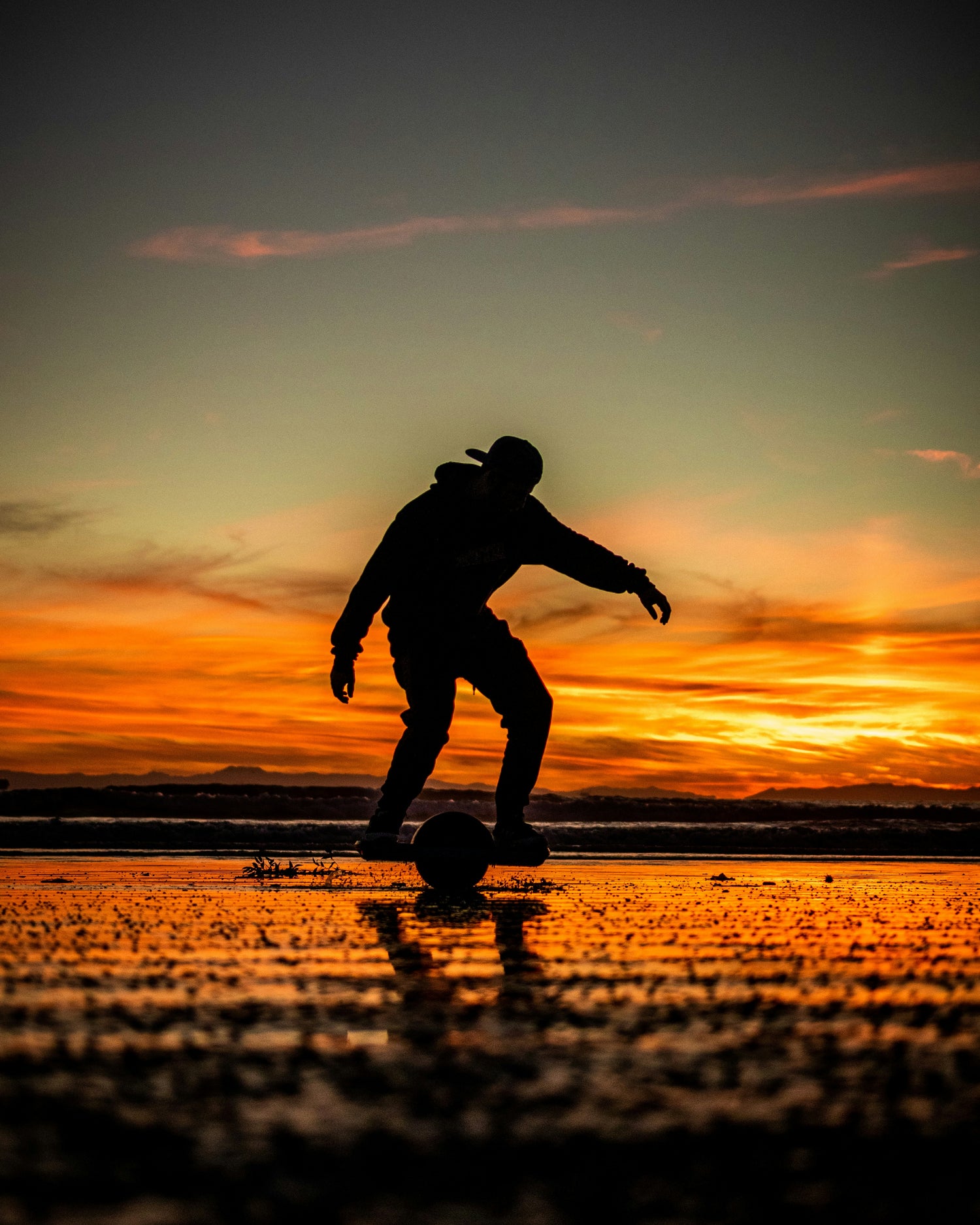 a man riding a onewheel on the beach during sunset
